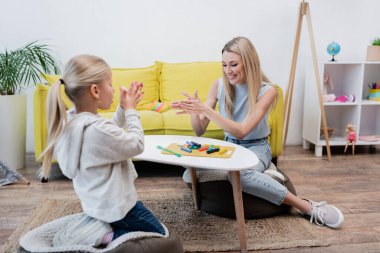 Smiling woman warming plasticine near blurred kid at home 