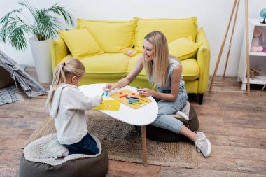Positive woman holding plasticine near kid at home 