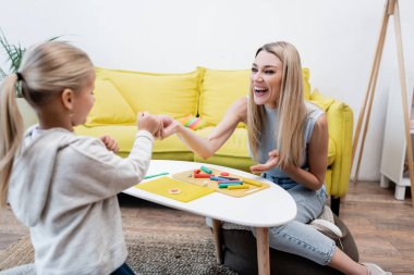 Positive parent pointing at plasticine near daughter and coffee table at home 
