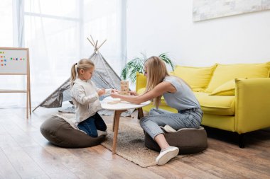 Mother and daughter playing wood blocks game at home 