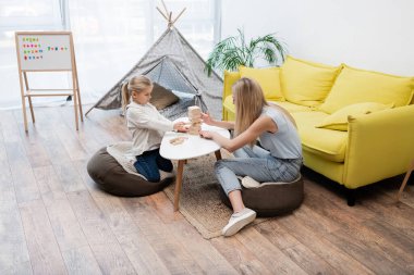 Kid and mother playing wood blocks game on coffee table at home 