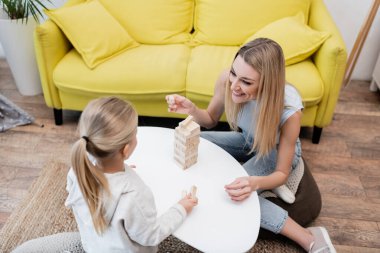 High angle view of smiling parent holding wooden block near child at home 
