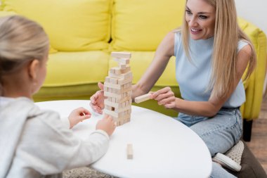 Woman playing wood blocks game with blurred daughter at home 