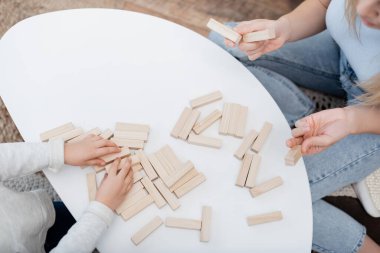 Cropped view of mother holding wooden blocks near kid and coffee table at home 