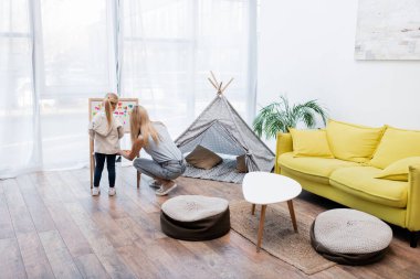 Back view of family playing with magnetic easel near teepee at home 