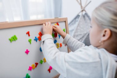 Blurred girl playing with magnets on easel at home 