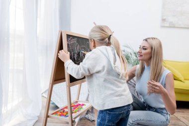 Kid drawing on chalkboard near parent at home 