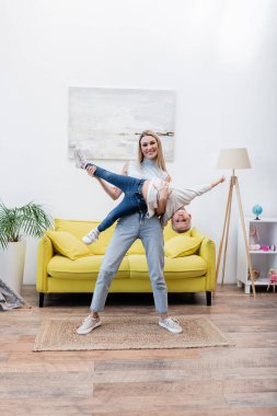 Smiling mom lifting daughter and looking at camera at home 