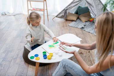 High angle view of woman and kid applying paint on hands at home 