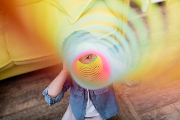 Kid looking at camera through slinky at home 