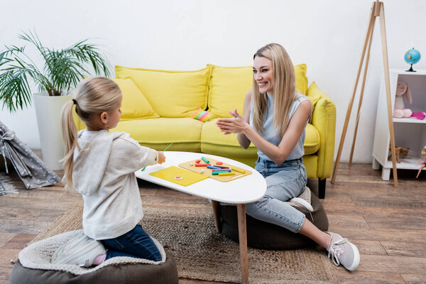 Smiling parent warming plasticine near daughter and coffee table at home 