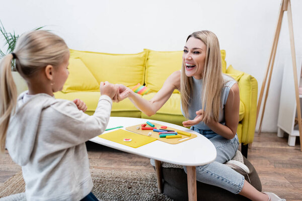 Positive parent pointing at plasticine near daughter and coffee table at home 