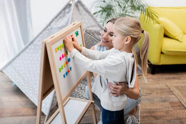 Smiling Mother Hugging Kid Magnetic Easel Blurred Tent Home — Fotografia de Stock