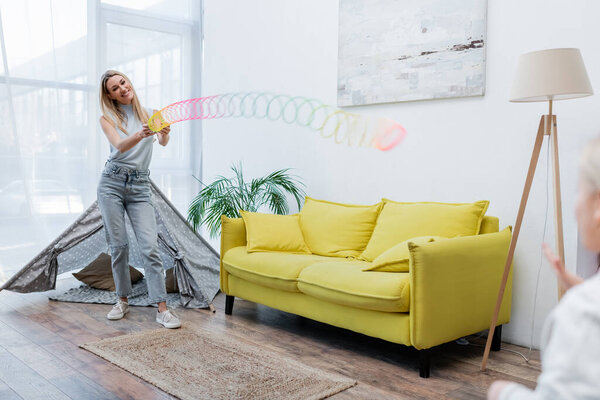 Smiling woman playing with slinky and child in living room 