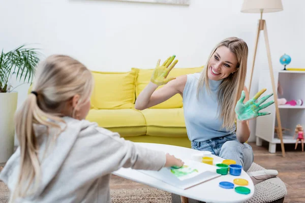 Smiling Woman Showing Hands Paint Blurred Kid Home — Foto Stock