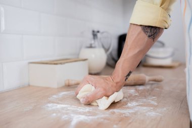 Dövmeli bir adamın mutfakta mangır hazırlarken çekilmiş görüntüsü. 