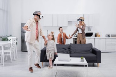 VR kulaklıklı çift mutfakta oynarken torunlarıyla el ele tutuşuyor.