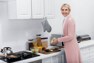 Neşeli orta yaşlı kadın elinde marul tutarken taze sebze salatası hazırlıyor.