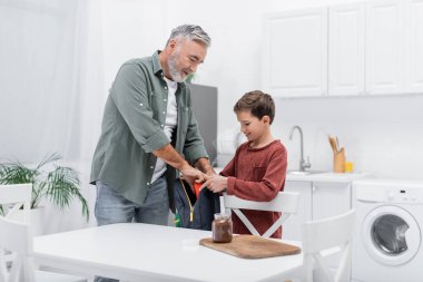 Son sınıf öğrencisi, torunun çantasının yanına çikolata ezmesi koymasına yardım ediyor.