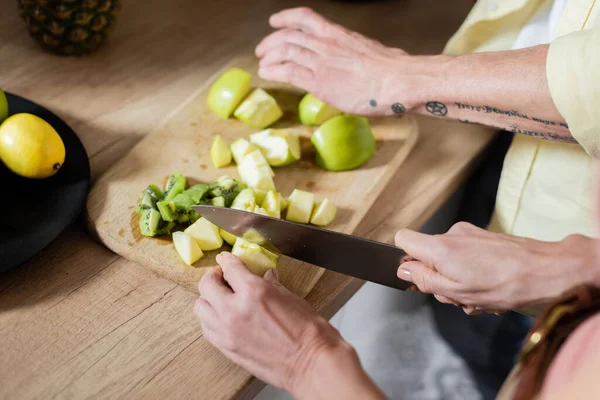 Cropped View Mature Woman Cutting Apple Tattooed Husband Kitchen — Stock Photo, Image