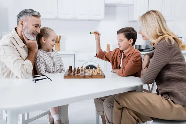 Niño Sosteniendo Figura Ajedrez Cerca Abuelos Sonrientes Hermana Cocina — Foto de Stock