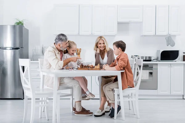 Senior Man Pointing Finger While Playing Chess Wife Grandchildren — Stock Photo, Image