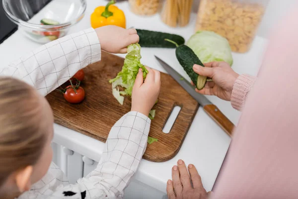 top view of cropped granny and granddaughter near fresh vegetables and chopping board