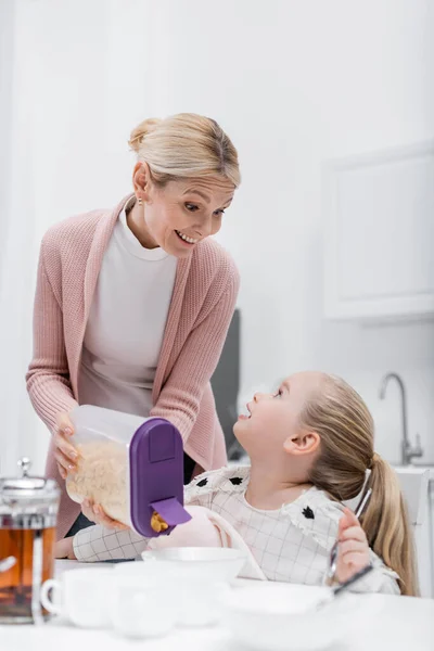 Happy Middle Aged Woman Holding Container Corn Flakes Granddaughter Kitchen — Stock Photo, Image