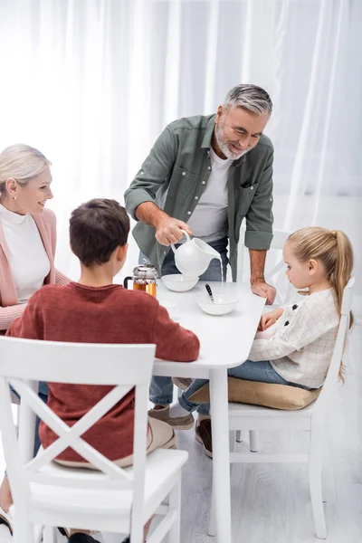 Smiling Senior Man Pouring Milk Breakfast Wife Grandchildren — Stock Photo, Image