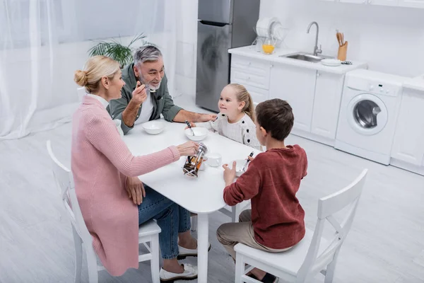 Veselý Muž Mluví Vnoučaty Blízkosti Manželky Nalévání Čaje Při Snídani — Stock fotografie