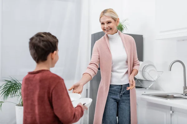 Boy Giving Bowls Pleased Granny Standing Sink Kitchen — Stock Photo, Image