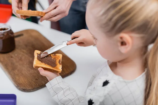 Chica Borrosa Difundir Pasta Chocolate Tostadas Mientras Ayuda Abuela Preparar — Foto de Stock