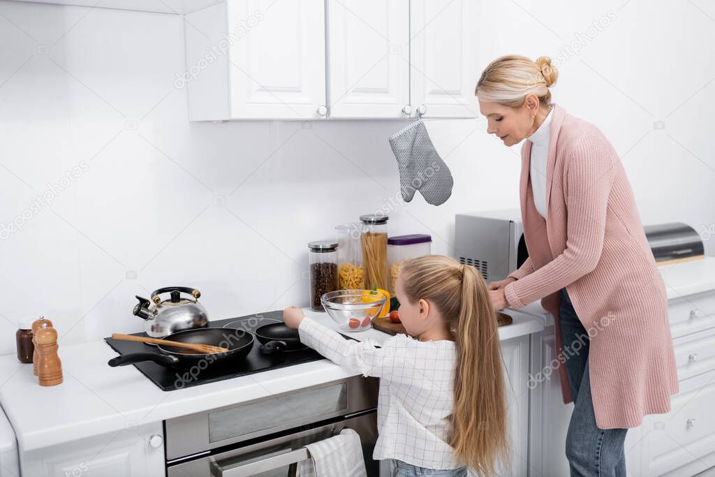 little girl helping grandmother cooking in kitchen