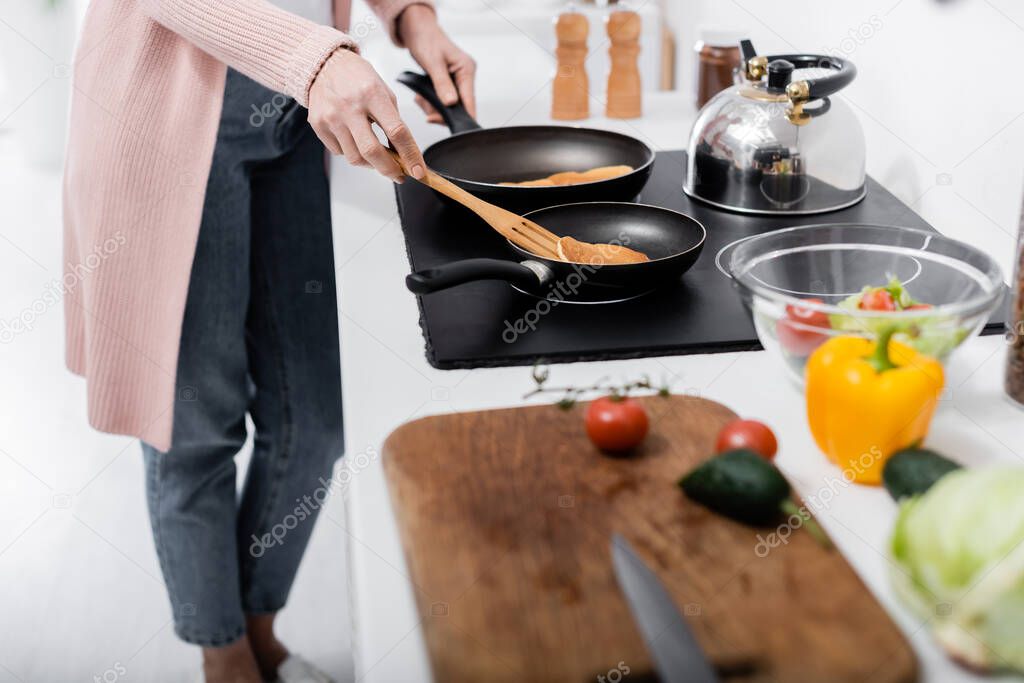 partial view of woman cooking pancakes near fresh vegetables on blurred foreground