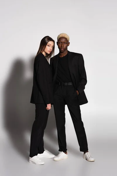 ブロンドアフリカ系アメリカ人男性とブルネット女性の完全な長さビューで黒スーツでグレーと影 — ストック写真