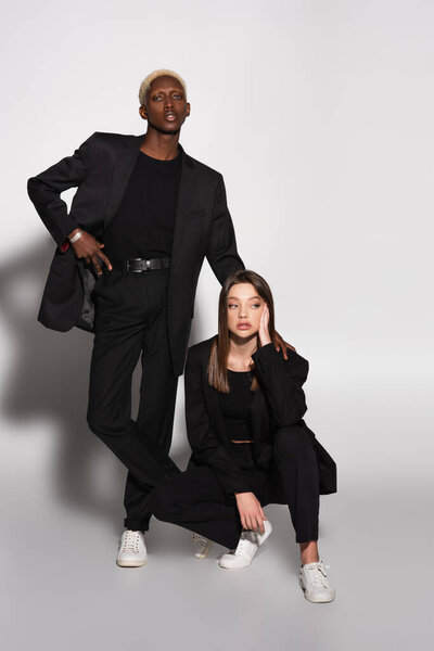 блондинка африканский американец с рукой на поясе рядом с молодой брюнеткой женщина на сером с тенью