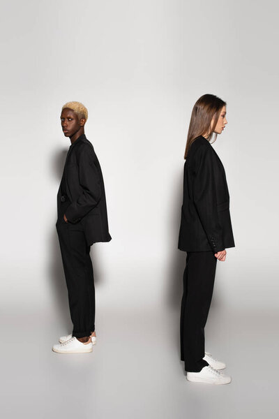 Африканский американец с отбеленными волосами, стоящий с рукой в кармане рядом со стильной женщиной на сером с тенью