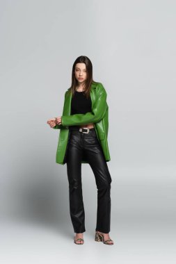 Deri pantolonlu ve ceketli esmer kadın gri üzerinde dikiliyor.