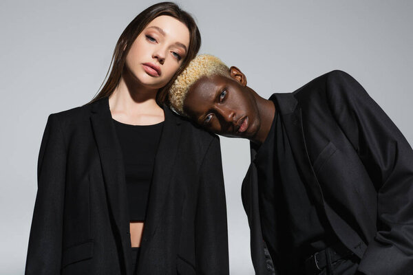 блондинка и стильный африканский американец, опирающийся на плечо брюнетки женщины, изолированной на сером