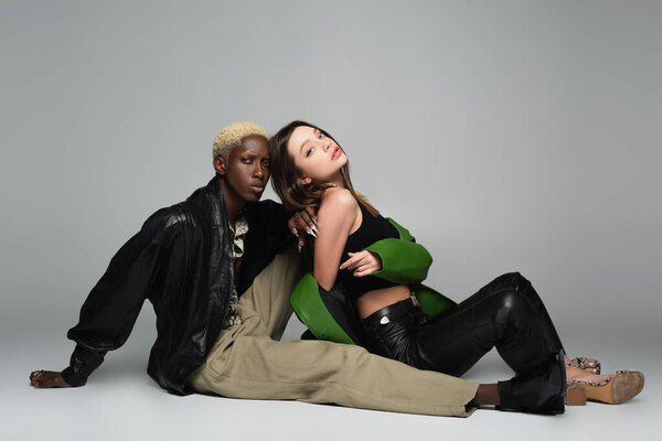 многонациональная пара в модной одежде, смотрящая в камеру, сидя на сером