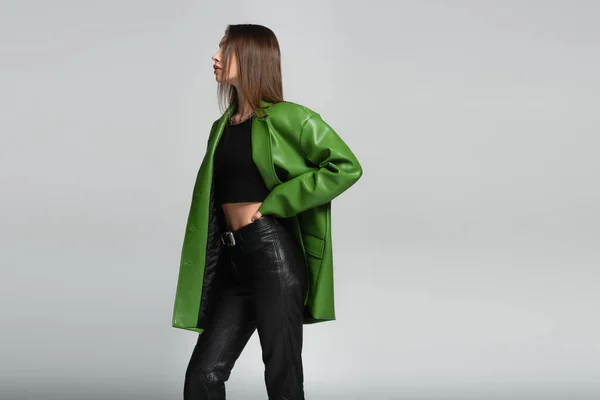 ブルネット女性で黒革のズボンと緑のジャケットPosingで手上の腰絶縁上グレー — ストック写真