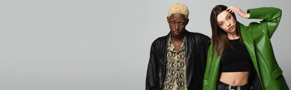красивая женщина в черном топе и зеленой куртке позирует рядом с блондинкой африканский американец мужчина изолирован на сером, баннер