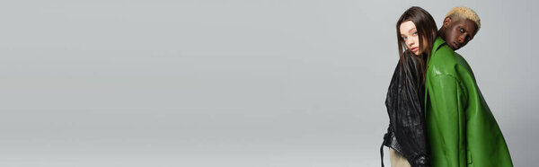 trendy interracial couple looking at camera while leaning on each other isolated on grey, banner