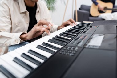 Cropped view of african american man playing synthesizer near blurred woman with acoustic guitar at home  clipart