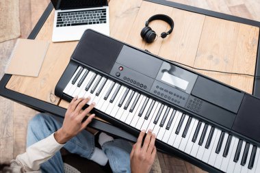 Cropped view of african american man playing synthesizer near headphones and laptop at home  clipart