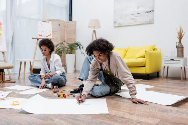 Positive African American Man Painting Paper Floor Girlfriend Home — Stock Photo, Image
