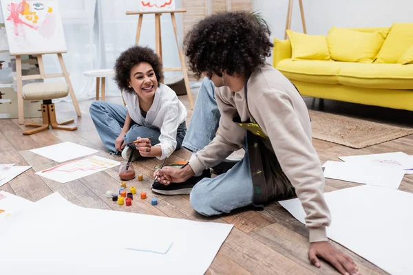 Sonriente Mujer Afroamericana Mirando Novio Cerca Pinturas Papeles Suelo Casa —  Fotos de Stock