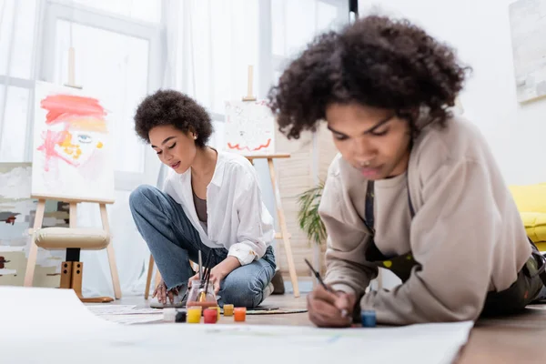 Mujer Afroamericana Pintando Sobre Papel Cerca Novio Borroso Suelo Sala — Foto de Stock