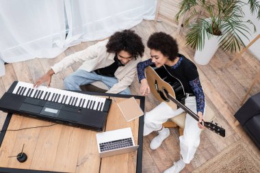 Evde dizüstü bilgisayarın yanında müzik aletleri çalan Afro-Amerikan çiftin genel görünümü 
