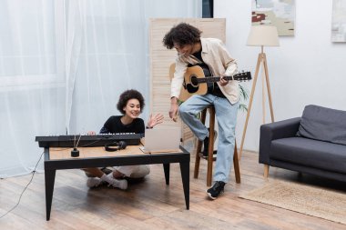 Evde bilgisayar başında müzik aletleri olan Afro-Amerikan bir çift var. 